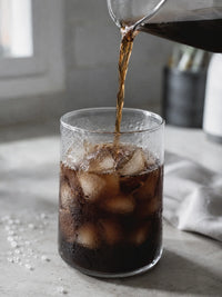 Thumbnail for Pouring iced coffee into a glass with ice cubes on a light surface.
