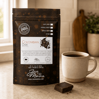 Thumbnail for Coffee package labeled 'Colombian Dark Roast' by Java Momma with a cup of coffee and chocolate on a table.
