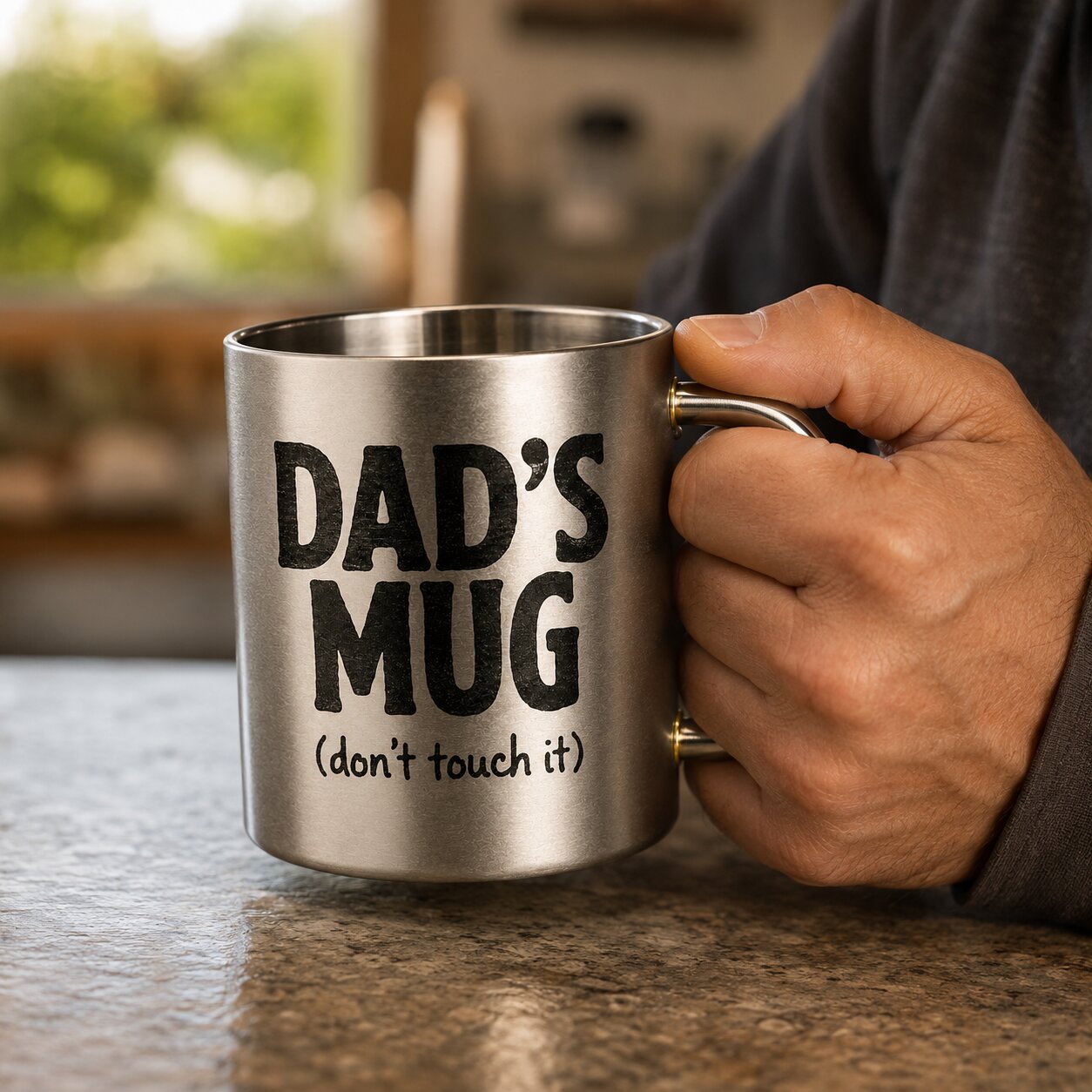 Hand holding a silver mug with 'DAD'S MUG (don't touch it)' text in a kitchen setting.