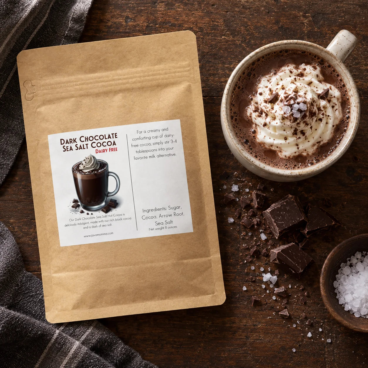 Dairy Free Dark Chocolate Sea Salt Hot Cocoa Mix packaging next to a cup of hot cocoa topped with whipped cream.