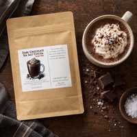 Thumbnail for Dairy Free Dark Chocolate Sea Salt Hot Cocoa Mix packaging next to a cup of hot cocoa topped with whipped cream.