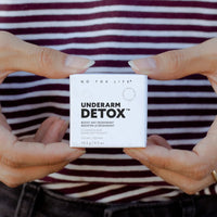 Thumbnail for Close-up of hands holding a small white box labeled No Tox Life Underarm Detox – Deodorant Booster Cleansing Bar (19.3g) in front of a person in a maroon and white striped shirt. Ideal for those switching to natural deodorant.