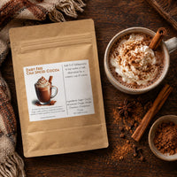Thumbnail for Dairy Free Dark Chai Spiced Hot Cocoa Mix package next to a mug of hot cocoa topped with whipped cream and spices.