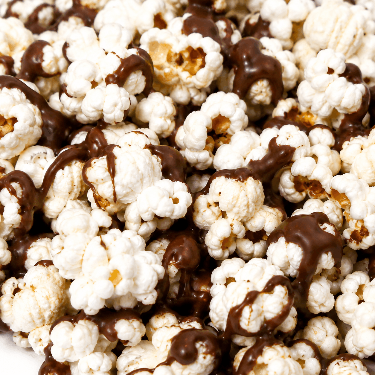 Close-up of white popcorn kernels drizzled with dark chocolate, filling the frame.