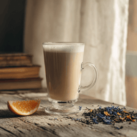 Thumbnail for London Fog latte made with Earl Grey tea, steamed milk, and vanilla in a clear glass mug beside orange slice and loose tea.