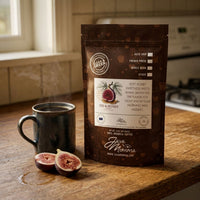 Thumbnail for Java Momma Fig & Honey Coffee bag on a wood kitchen counter beside a steaming dark ceramic mug and two halved fresh figs