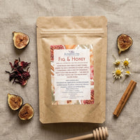 Thumbnail for Fig & Honey loose leaf herbal tea bag on a linen surface surrounded by fresh and dried fig halves, dried hibiscus petals, chamomile flowers, cinnamon sticks, and a honey dipper