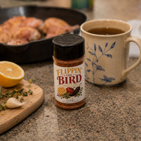Thumbnail for Flippin' the Bird spice blend on a kitchen counter with a mug, lemon, and herbs.