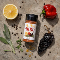 Thumbnail for Spice jar labeled 'Flippin' the Bird' surrounded by peppers, lemon, and herbs on a concrete surface