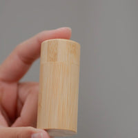 Thumbnail for A hand displays the Bamboo Floss Holder with Charcoal Floss—an eco-friendly, gentle, and refillable oral care product—against a plain gray background, showcasing its smooth, natural finish.