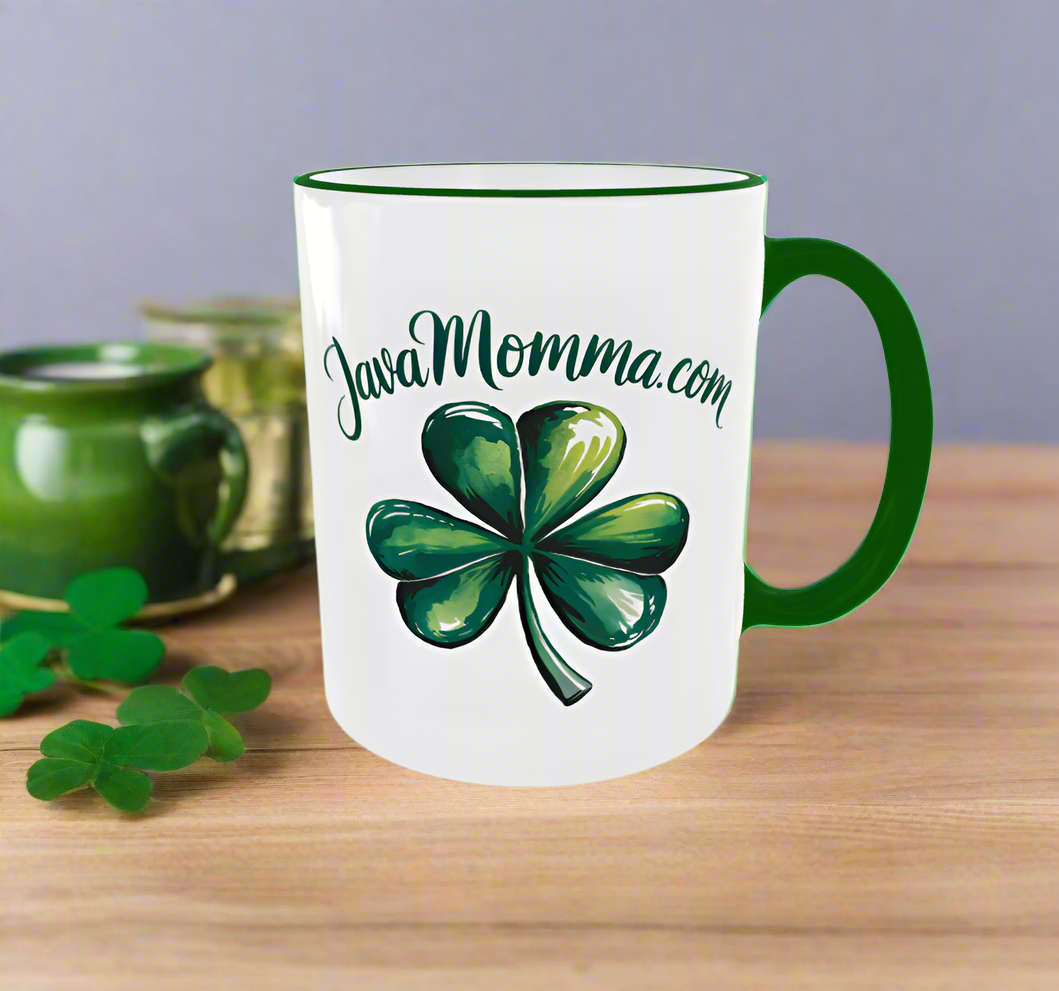 A festive St. Patrick’s Day mug featuring a bold green shamrock and the JavaMomma.com logo in stylish script. The mug has a white base with a green handle and rim, perfectly complementing the lucky Irish theme. Set against a cozy wooden backdrop with green mugs and fresh shamrocks, it's the ultimate way to sip in style this St. Paddy’s season! 