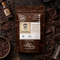 Thumbnail for A brown coffee pouch labeled 'Java Momma' and 'Frank & Finest Chocolate Coffee' is photographed flat on a dark textured surface with chocolate pieces, a small labeled glass bottle, and coffee beans around it. No person or animal is present, so this is Product/Packaging rather than Lifestyle.