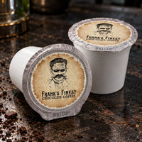 Thumbnail for Two white coffee pods in foil cups on a dark countertop, with one pod lying on its side and the other standing upright. Both have tan circular labels reading 