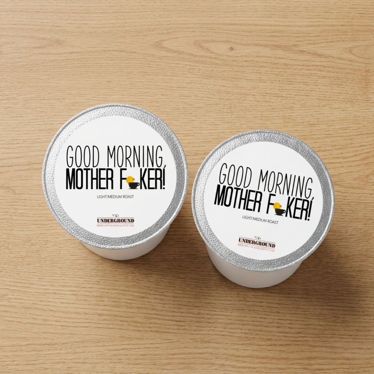 Two coffee pods with 'Good Morning, Mother F**ker!' text on a wooden surface