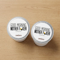 Thumbnail for Two coffee pods with 'Good Morning, Mother F**ker!' text on a wooden surface