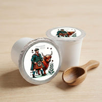 Thumbnail for Two Highlandder Grogg coffee pods with Scottish-themed illustrations and a wooden scoop on a beige background
