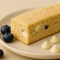 Thumbnail for A rectangular piece of Huckleberry White Chocolate Biscotti – Sweet, Tart & Soft-Bite Perfect, garnished with chocolate chips and fresh blueberries on a beige plate, reminiscent of handcrafted biscotti.