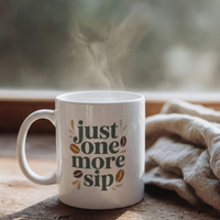 Thumbnail for Steaming hot coffee in a 'Just one more sip' mug sitting on a wooden window sill next to a cozy beige blanket.