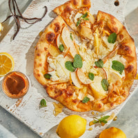 Thumbnail for A rustic pizza with ricotta, pear, fresh mint, and Lemon Vanilla Honey Cream Spread 🍋 – Tart, Sweet & Totally Irresistible sits on a white wooden board with lemons, vanilla beans, and a dish of spice paste.