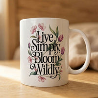 Thumbnail for White mug with 'Live Simply, Bloom Wildly' text and floral designs on a wooden surface.