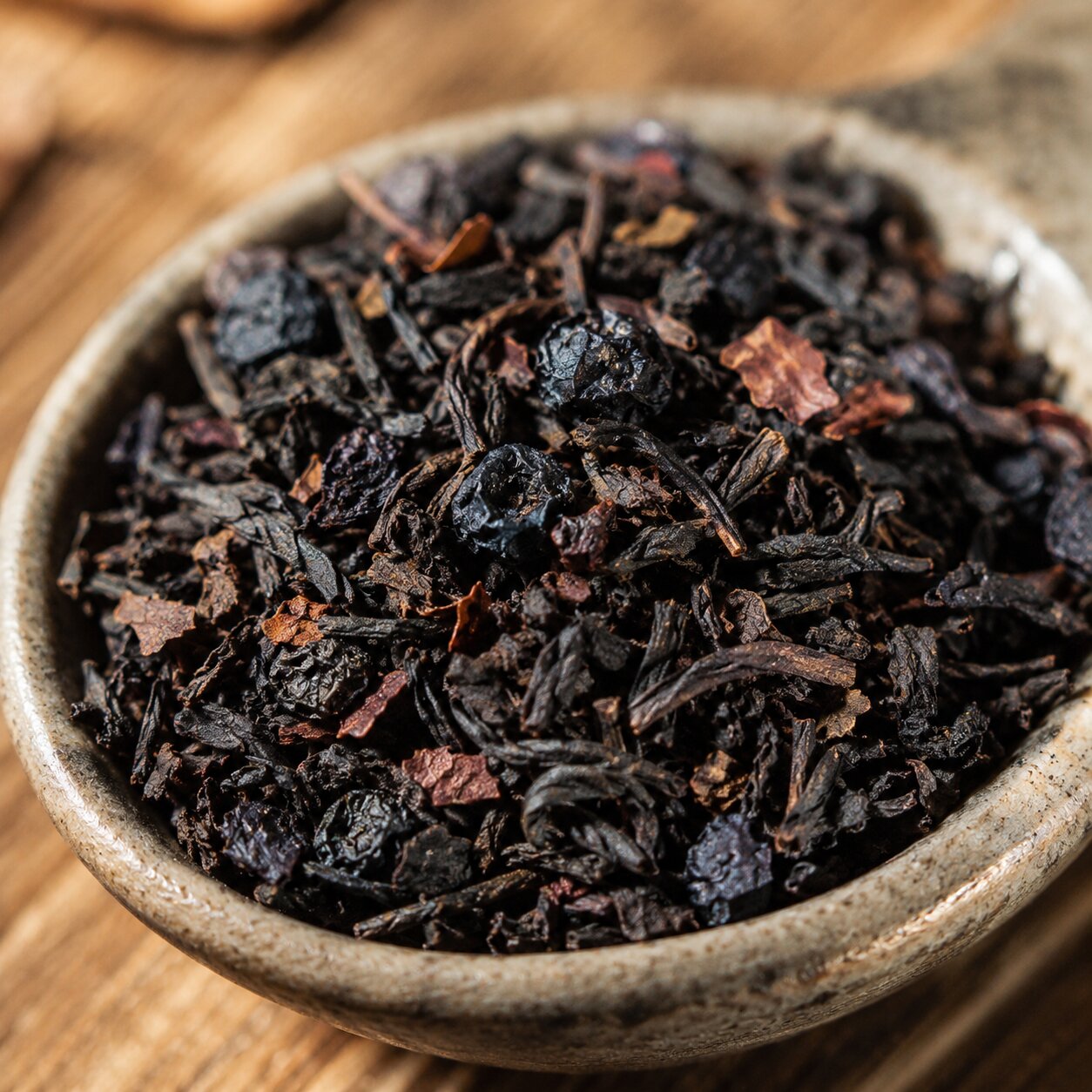 Close-up of dried black tea leaves in a ceramic bowl on a wooden surface
