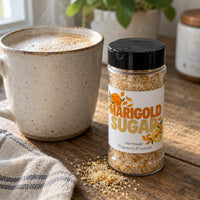 Thumbnail for Marigold Sugar Sprinkle jar beside a steaming cup, showcasing vibrant sugar mix with floral and citrus accents.