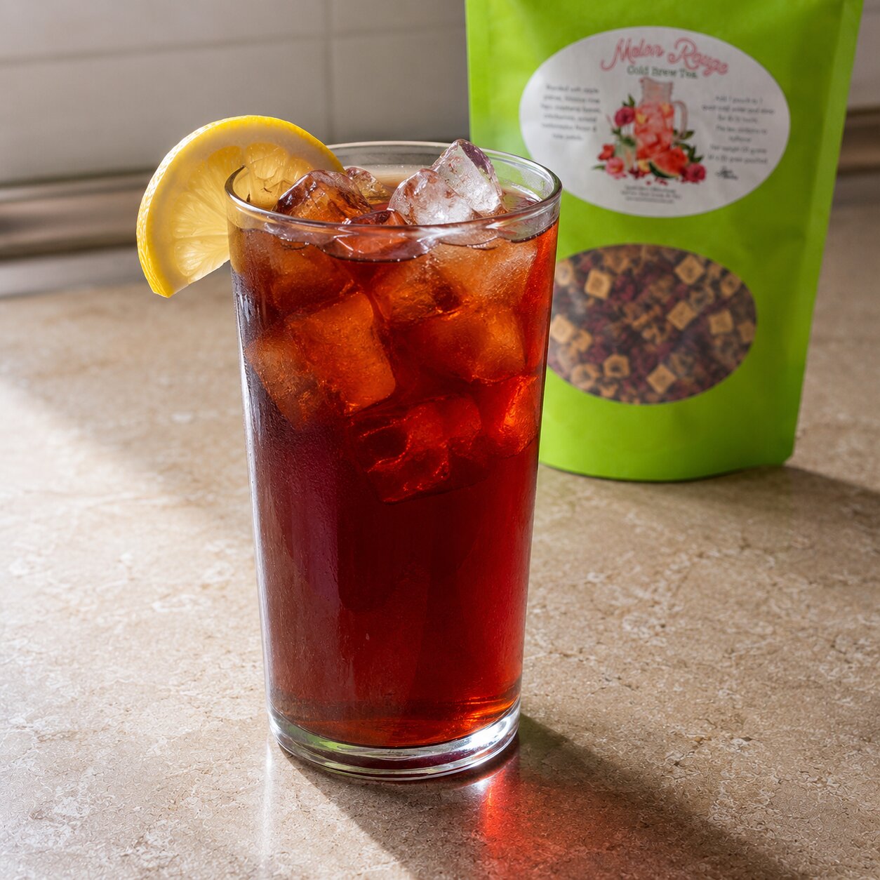 Glass of iced tea with a lemon wedge next to a green bag of tea leaves on a countertop.