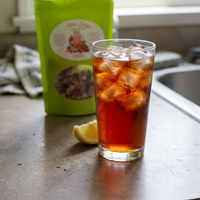 Thumbnail for Glass of melon rougee iced tea with a green bag of tea leaves on a kitchen counter.e 
