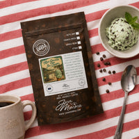 Thumbnail for Java Momma Mint Chocolate Chip Ice Cream coffee package with a bowl of mint chocolate chip ice cream and a cup of coffee on a red and white striped tablecloth.