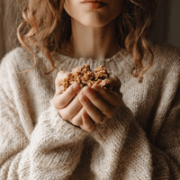 Thumbnail for A person in a cozy beige sweater gently cradles My Sister’s Granola – Nutty, Sweet, and Totally Addictive – in their hands, with curly hair framing their partially visible face as the focus stays on the granola.
