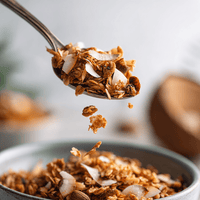 Thumbnail for A close-up of a spoonful of My Sister’s Granola – Nutty, Sweet, and Totally Addictive, featuring oats, coconut flakes, and nuts above a bowl of more granola, with some pieces falling from the spoon.
