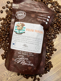 Thumbnail for A bag of Java Momma Pecan Praline – a buttery, nutty medium roast inspired by a Southern summer treat and keto friendly – rests on a surface with scattered beans. The bag shows a coffee cup with pecans and an ice cream swirl.