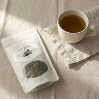 Thumbnail for Plot Twist Mint Tea | Darjeeling & Peppermint Black Tea Blend package beside a cup of brewed tea on a soft linen backdrop.