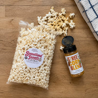Thumbnail for Bag of popcorn with a Sensational Sweets label and a bottle of Sweet Corn Blend seasoning on a wooden surface.