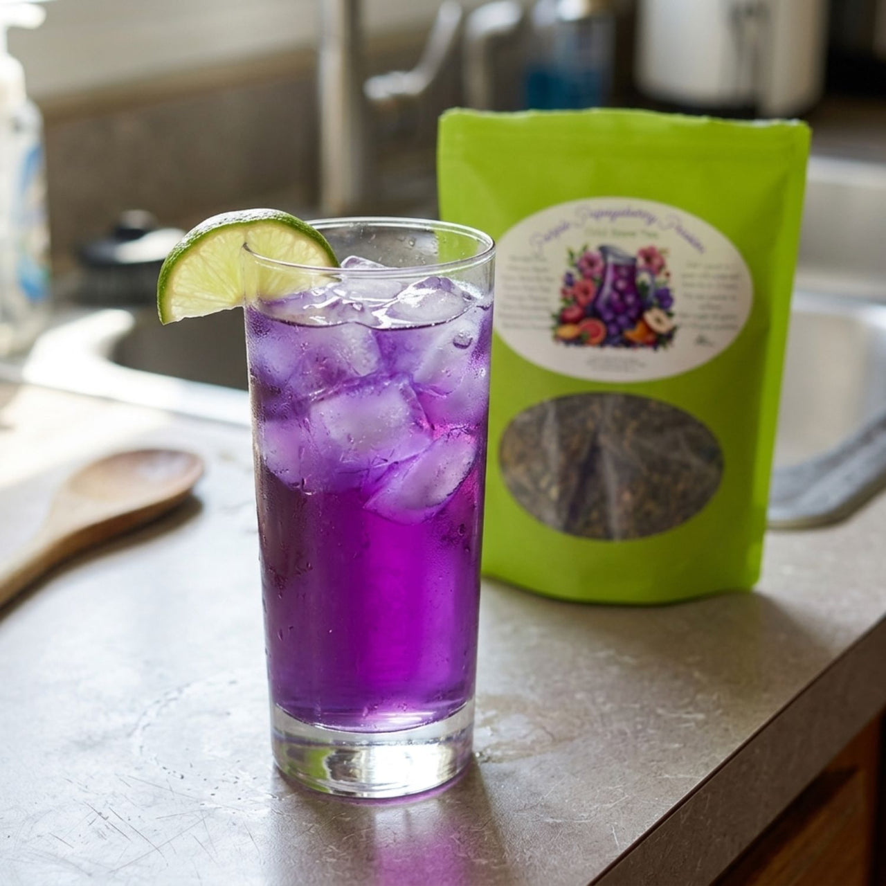 Purple iced drink in a glass with a lime wedge, next to a green bag of tea on a kitchen counter.