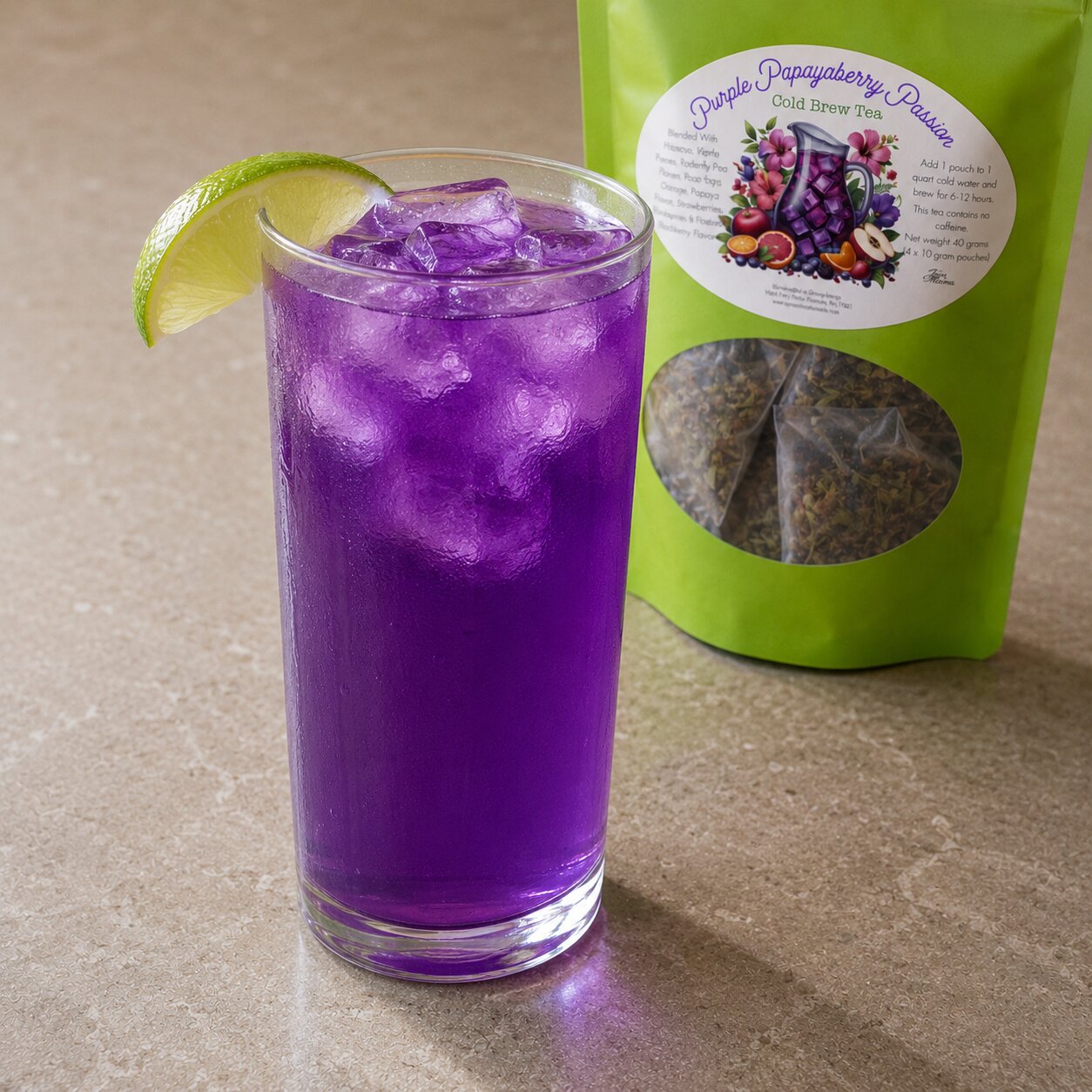 Purple iced drink in a glass with a lime wedge next to a green package of 'Purple Papayaberry' tea.