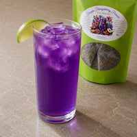 Thumbnail for Purple iced drink in a glass with a lime wedge next to a green package of 'Purple Papayaberry' tea.