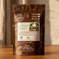 Thumbnail for Rainforest Crunch bag standing upright on a warm medium-toned wood surface. 
Background is a soft-focus linen or stone texture. Lighting is warm and directional — 
late afternoon window light.