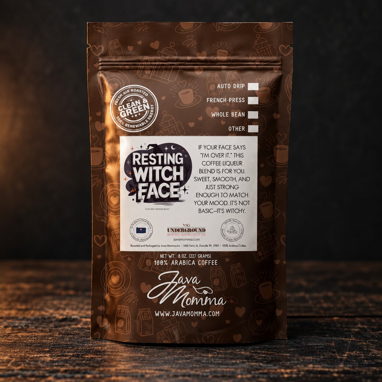 A stand-up pouch of Resting Witch Face+ coffee by Java Momma, set against a dark, moody background. The packaging is dark brown with white text and illustrations of coffee beans and hearts.