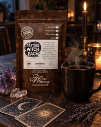 Thumbnail for A stand-up pouch of Java Momo 'Resting Witch Face' coffee is displayed on a rustic wooden table alongside a black ceramic mug, lit candles, tarot cards, and crystals in a cozy, atmospheric setting.