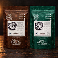 Thumbnail for Two stand-up coffee bags from Java Momma on a dark wooden surface. The left bag is brown with a white label and reads 'Resting Witch Face+' with 'Java Momma' below.