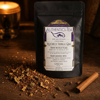 Thumbnail for Rooibos Vanilla Chai Tea package with a label on a wooden surface with tea leaves and a cinnamon stick.