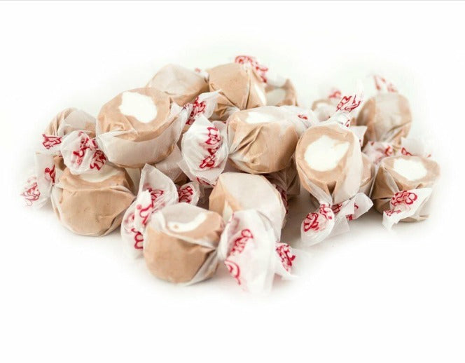 A pile of Root Beer Float Salt Water Taffy – Freeze-Dried Soda Shop Classic with a Crunch, brown candies with white centers in white wax paper wrappers, delivering nostalgic root beer float flavor in every crunchy bite.