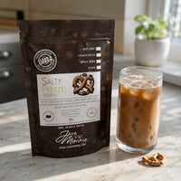 Thumbnail for Java Momma Salty Pretzel Cold Brew Pods bag beside a glass of iced coffee with a pretzel piece