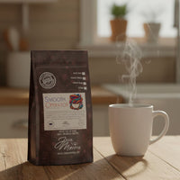 Thumbnail for A bag of Smooth Operator Mixed Roast Blend | Low Acid Coffee rests on a wooden table beside a steaming white mug, set against the backdrop of a cozy kitchen.
