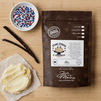 Thumbnail for Stars, Stripes & Sprinkles coffee bag on a wood surface surrounded by a bowl of red, white, and blue sprinkles, vanilla bean pods, and a scoop of buttercream frosting on parchment paper.