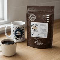 Thumbnail for Stars, Stripes & Sprinkles coffee bag on a wood counter beside a Spilling the Tea Since 1773 Java Momma mug and a filled ceramic coffee mug, natural window light.