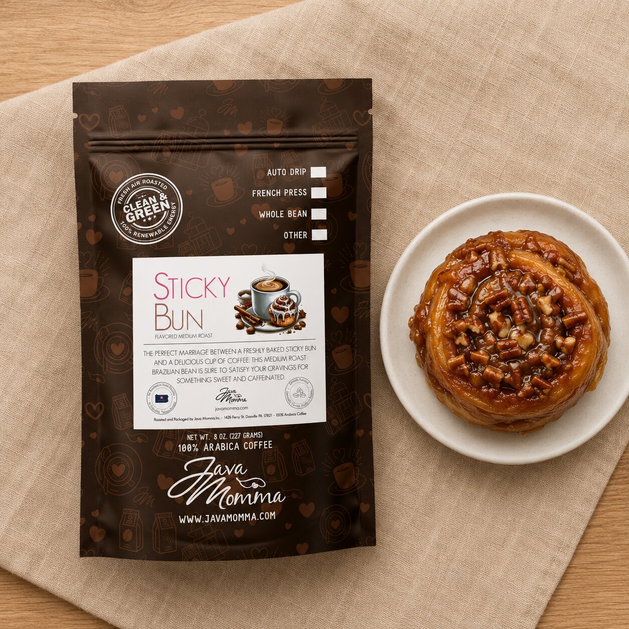 Java Momma coffee package labeled 'Sticky Bun' next to a sticky bun on a beige cloth.