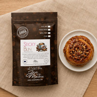 Thumbnail for Java Momma coffee package labeled 'Sticky Bun' next to a sticky bun on a beige cloth.