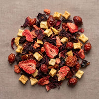Thumbnail for Overhead view of Strawberry Serendipity loose leaf herbal tea blend with dried strawberries, hibiscus petals, apple pieces, and rose hips on textured fabric.